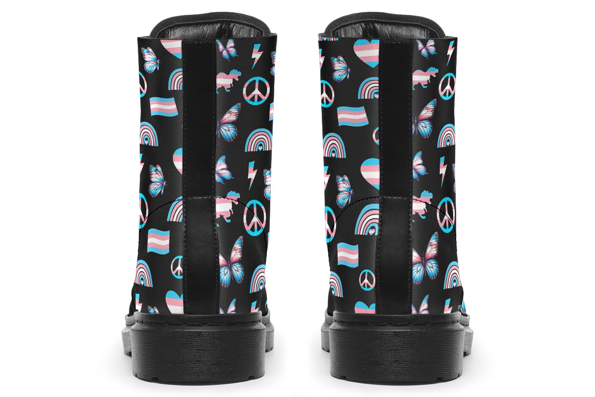 Black boots featuring a pattern of various icons in the trans flag colours, such as hearts, rainbows, peace signs, flags, butterflies and dinosaurs.
