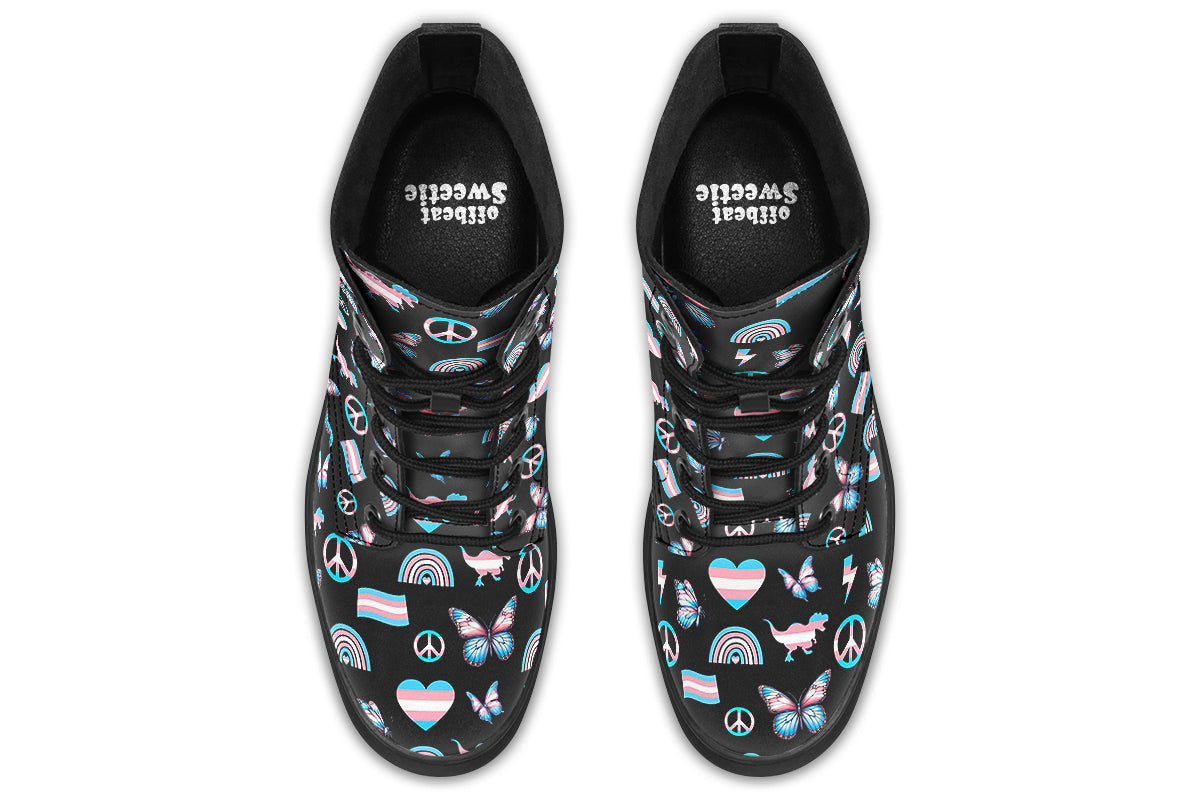 Black boots featuring a pattern of various icons in the trans flag colours, such as hearts, rainbows, peace signs, flags, butterflies and dinosaurs.