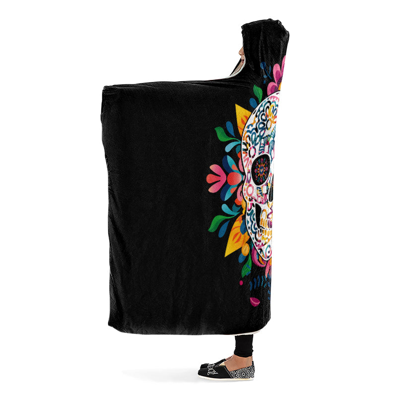Black hooded blanket with a colorful skull design, being worn by a person with arms outstretched. Side view.