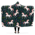 Hooded blanket with white and pink unicorn and leaves pattern on a dark green background.