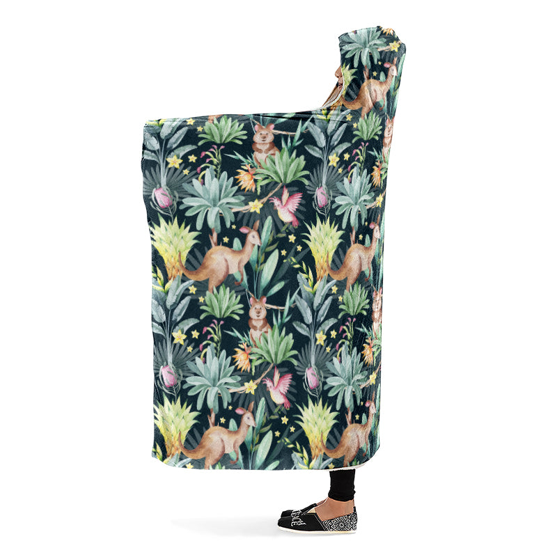 Person wearing a hooded blanket with an Australian animal pattern on a dark green background. The animals are kangaroos, quokkas and cockatoos. Side view.